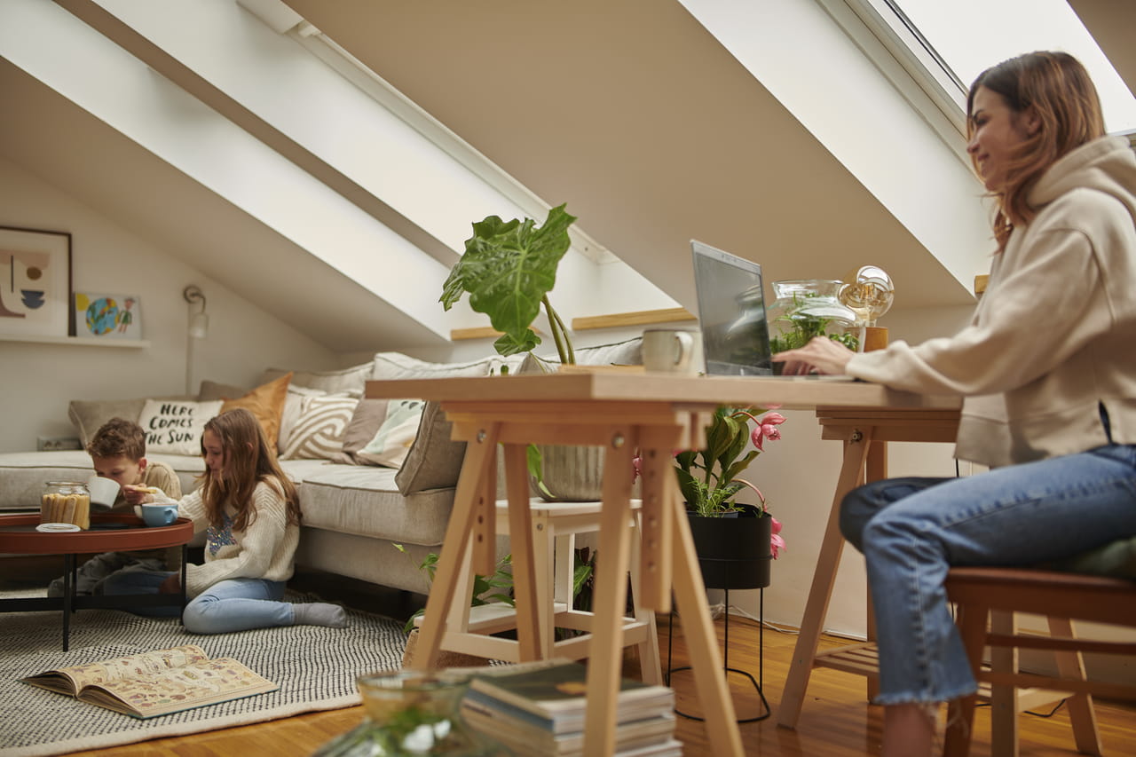 Hjemmekontor på loftet med VELUX-vindu, trepult, planter og koselig sitteområde.