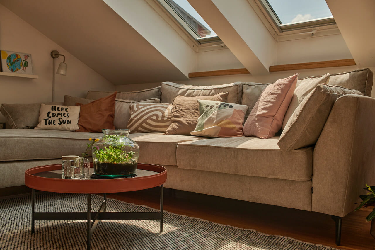 Sala de estar no sótão com sofá confortável, terrário na mesa e luz solar das janelas de telhado VELUX.