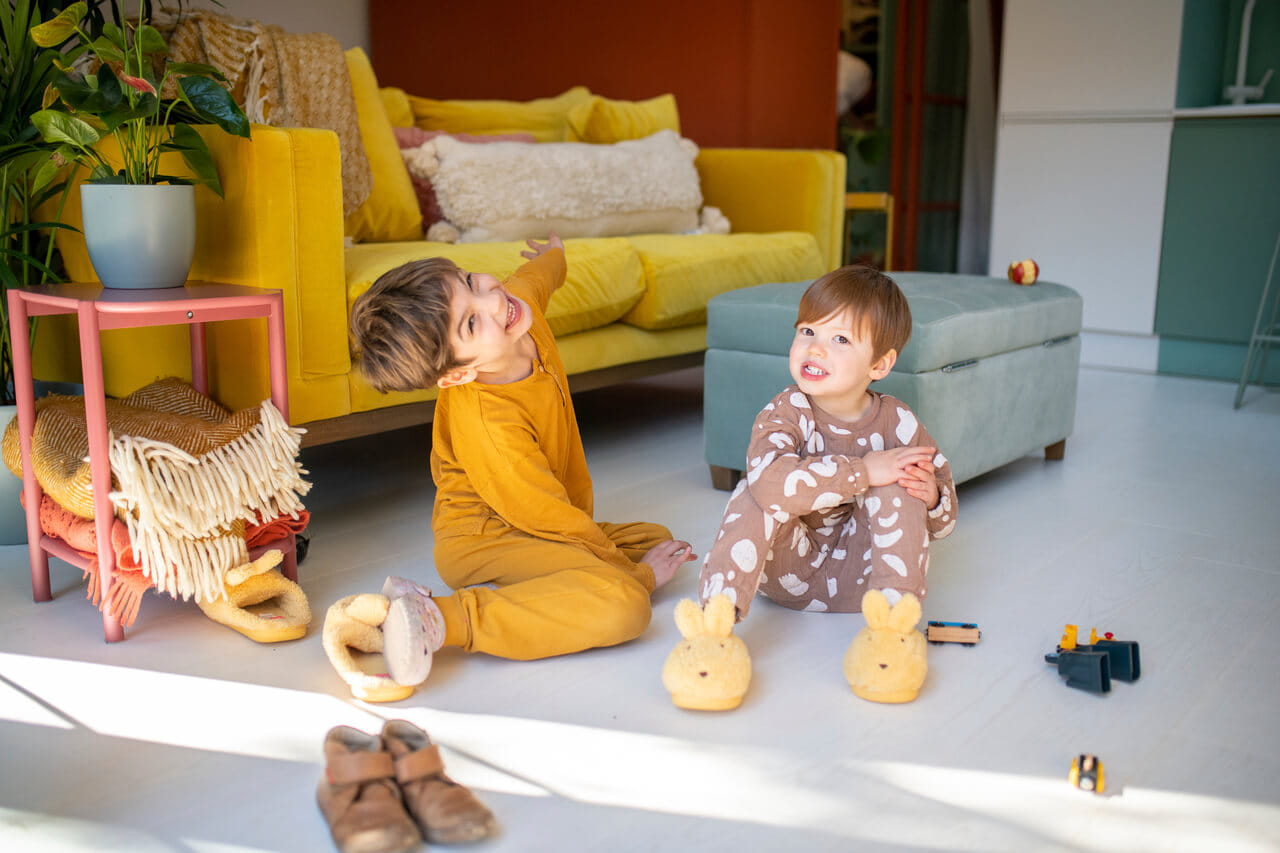 Des enfants jouent dans une salle de jeux lumineuse avec des meubles colorés et des jouets éparpillés sur le sol.