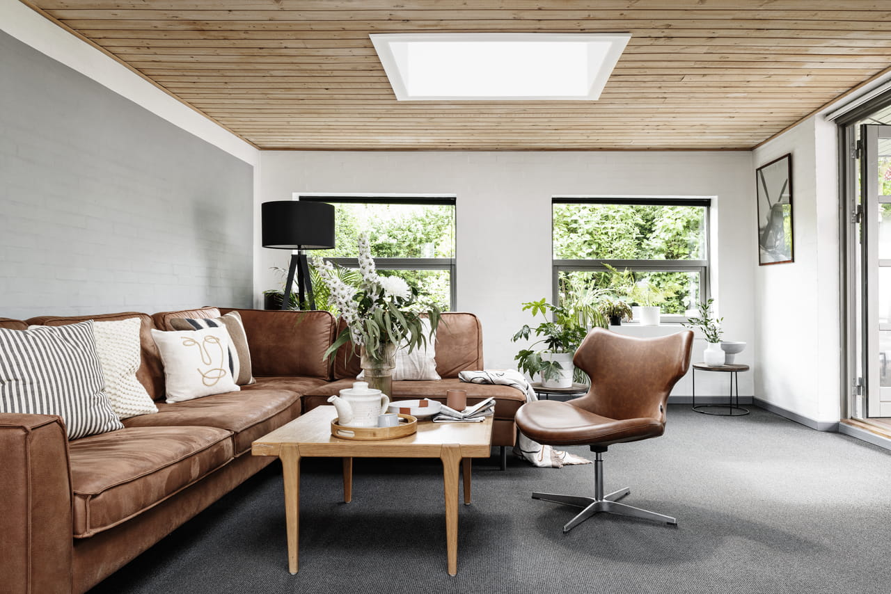 Chic modernt vardagsrum med lädersoffa, träbord, växter och VELUX takfönster.