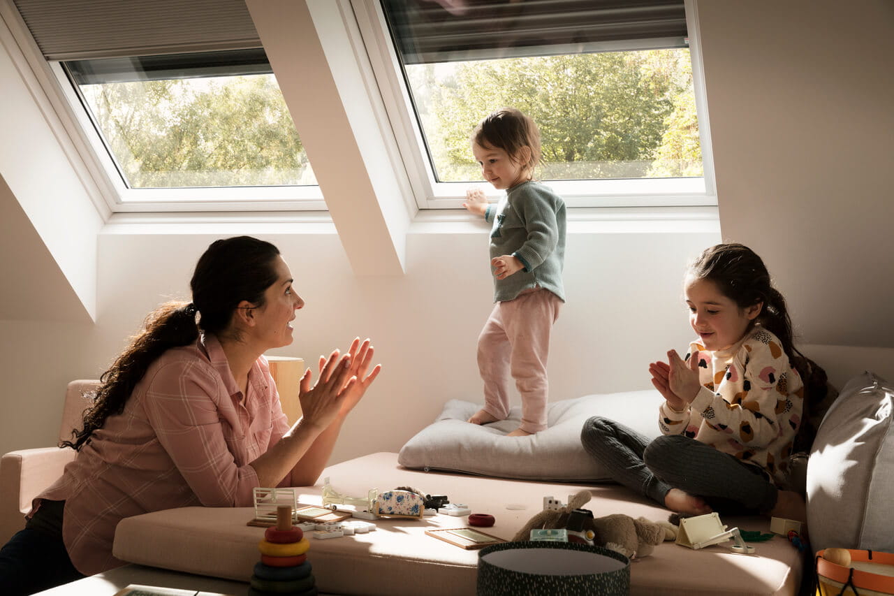 Kind speelt op zolderkamer met VELUX raam, volwassenen kijken toe.