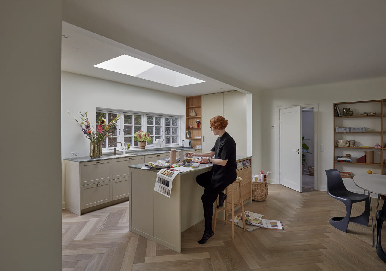 Kvinde læser ved køkkenø under et VELUX ovenlysvindue, med stilfuld indretning.