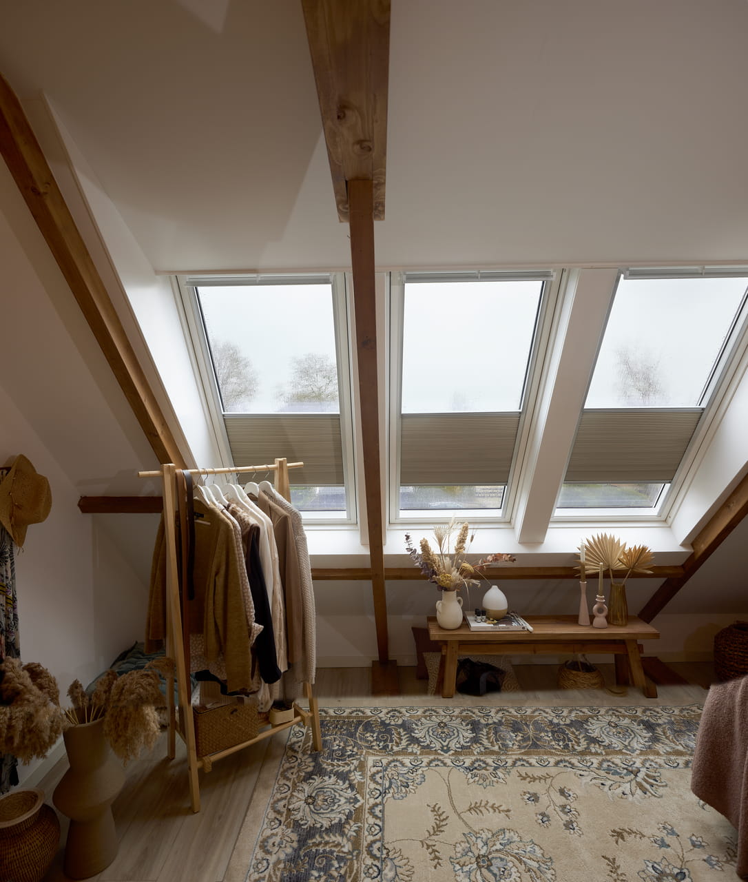 Zolder slaapkamer met houten balken en VELUX dakvenster, ingericht met kledingrek en bankje.