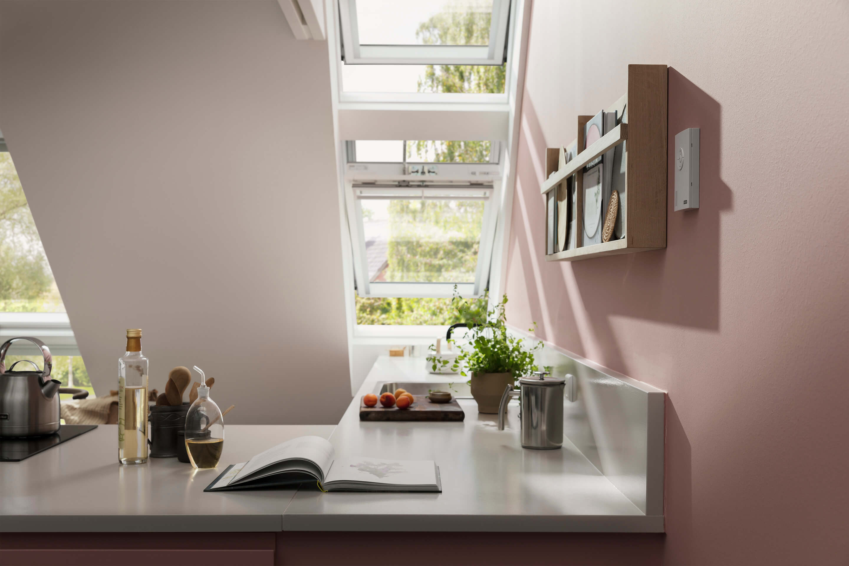 Cozinha moderna com janela de telhado VELUX, bancadas brancas e paredes cor-de-rosa.