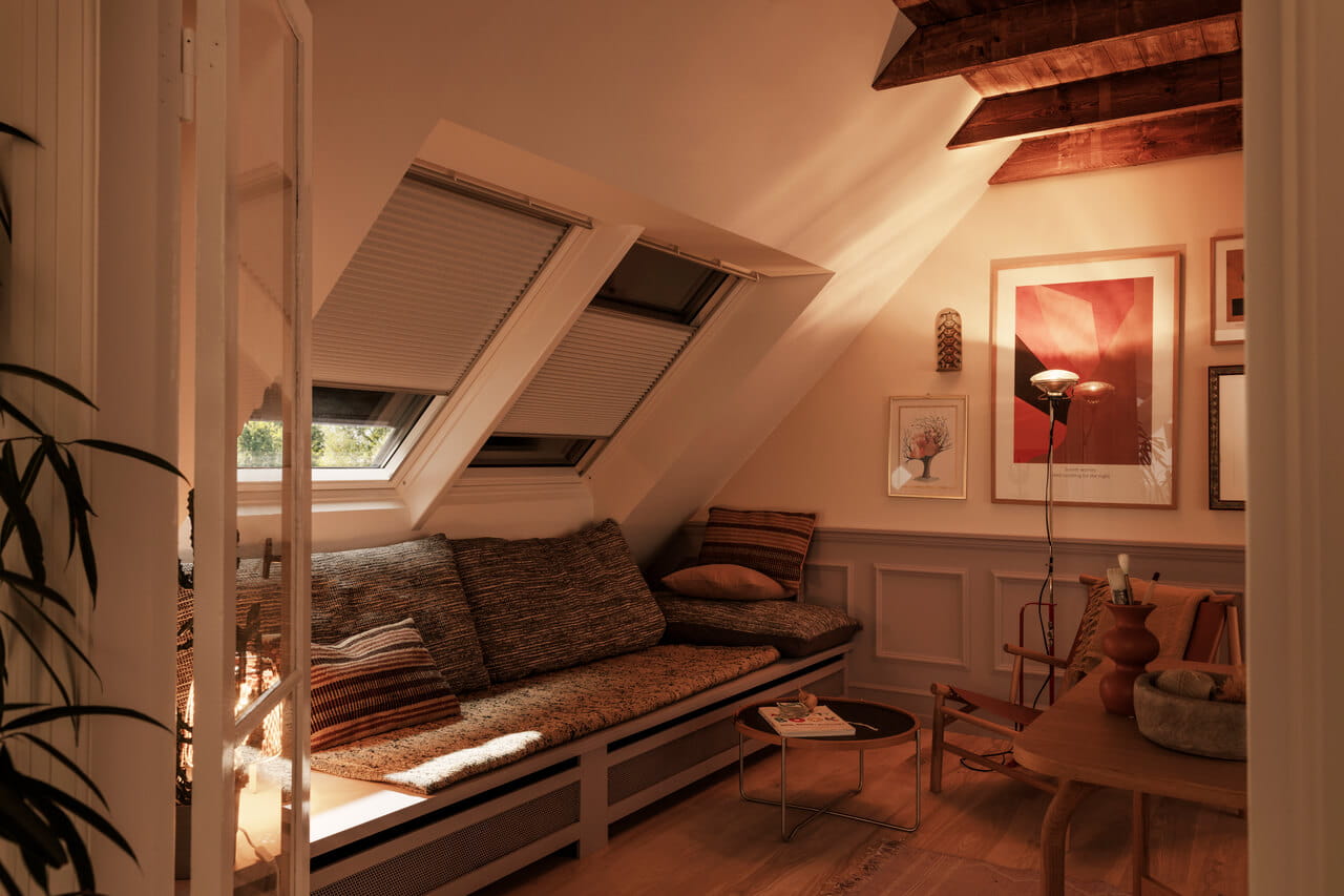 Espace de vie sous les combles avec lumière naturelle provenant des fenêtres de toit VELUX, poutres en bois et décoration cosy.