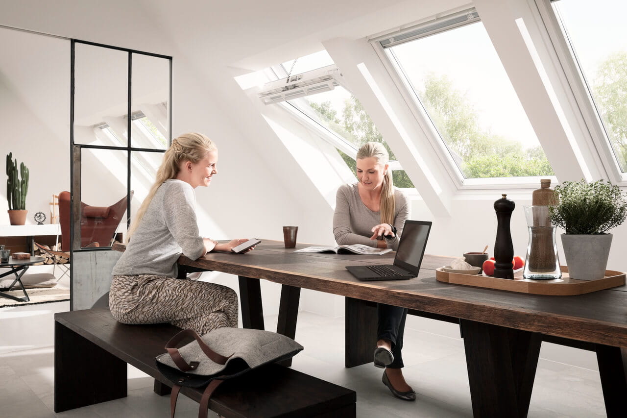 Bureau à domicile spacieux dans le grenier avec des fenêtres VELUX, une table en bois et une décoration minimaliste.