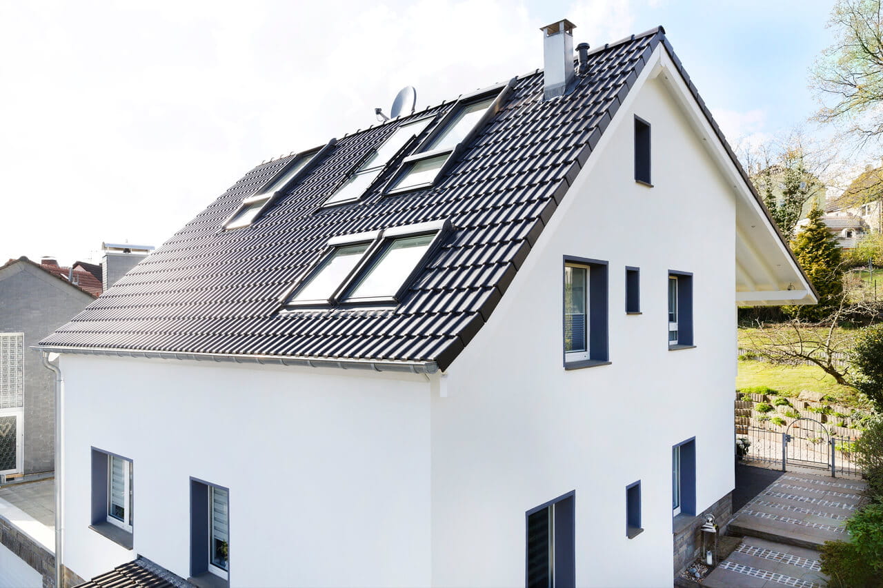 Casa unifamiliar moderna de color blanco con ventanas de tejado VELUX y entorno verde.