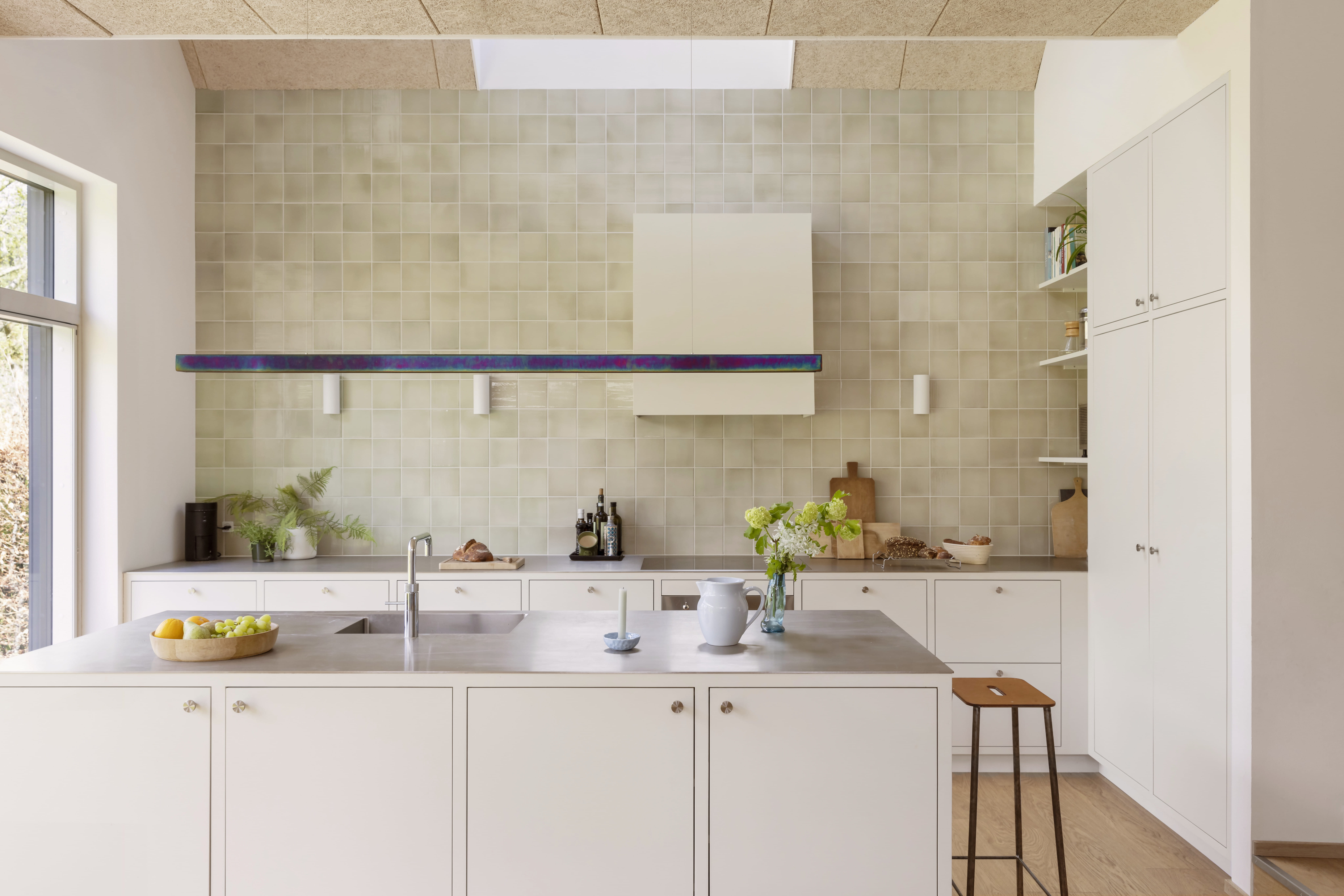 Ljus modernt kök med vita skåp, stålbänkskiva och ett VELUX takfönster.