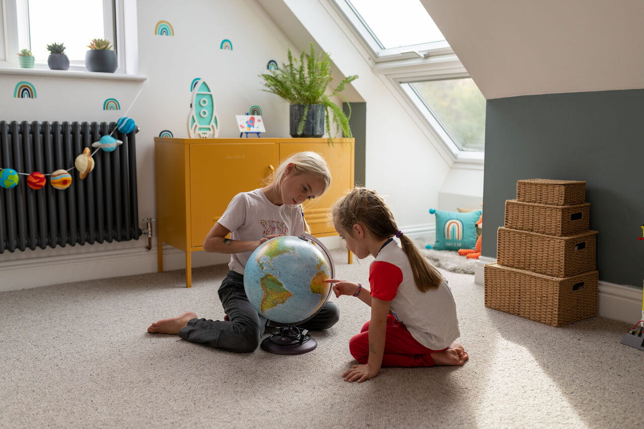 Children learning geography with a globe in a sunlit room with a VELUX skylight.
