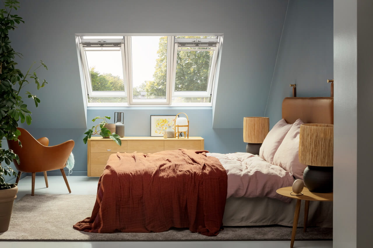 Dormitorio sereno con ventanas de tejado VELUX y ropa de cama terracota.