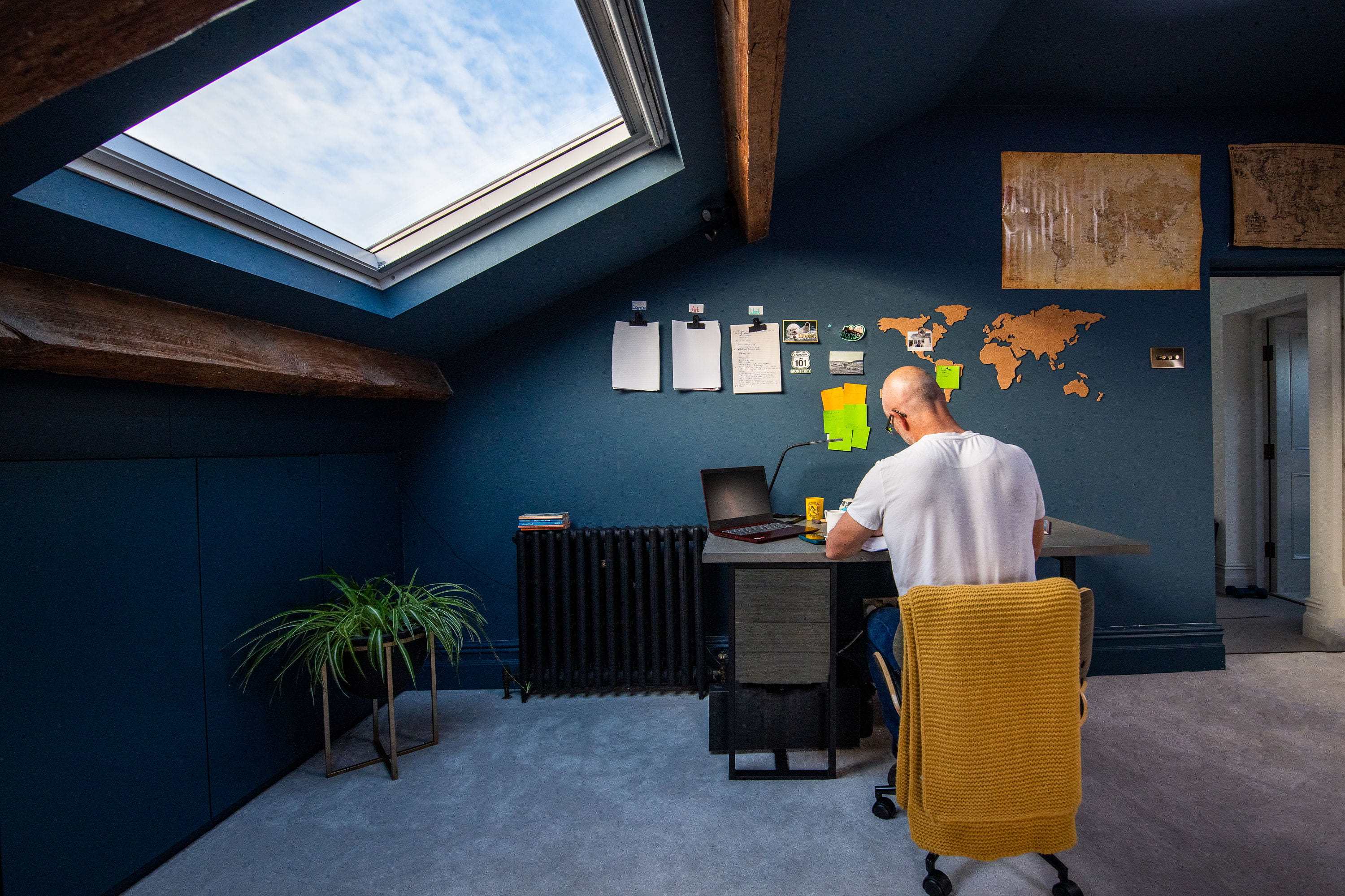 Home office with VELUX skylight, world map on wall, and man working at desk.