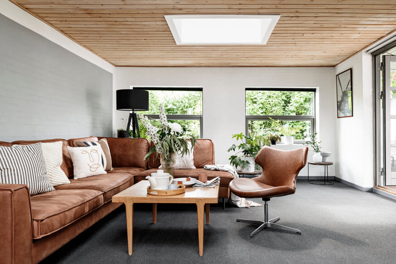 Moderne woonkamer met VELUX dakvenster, leren bank, houten accenten en kamerplanten.