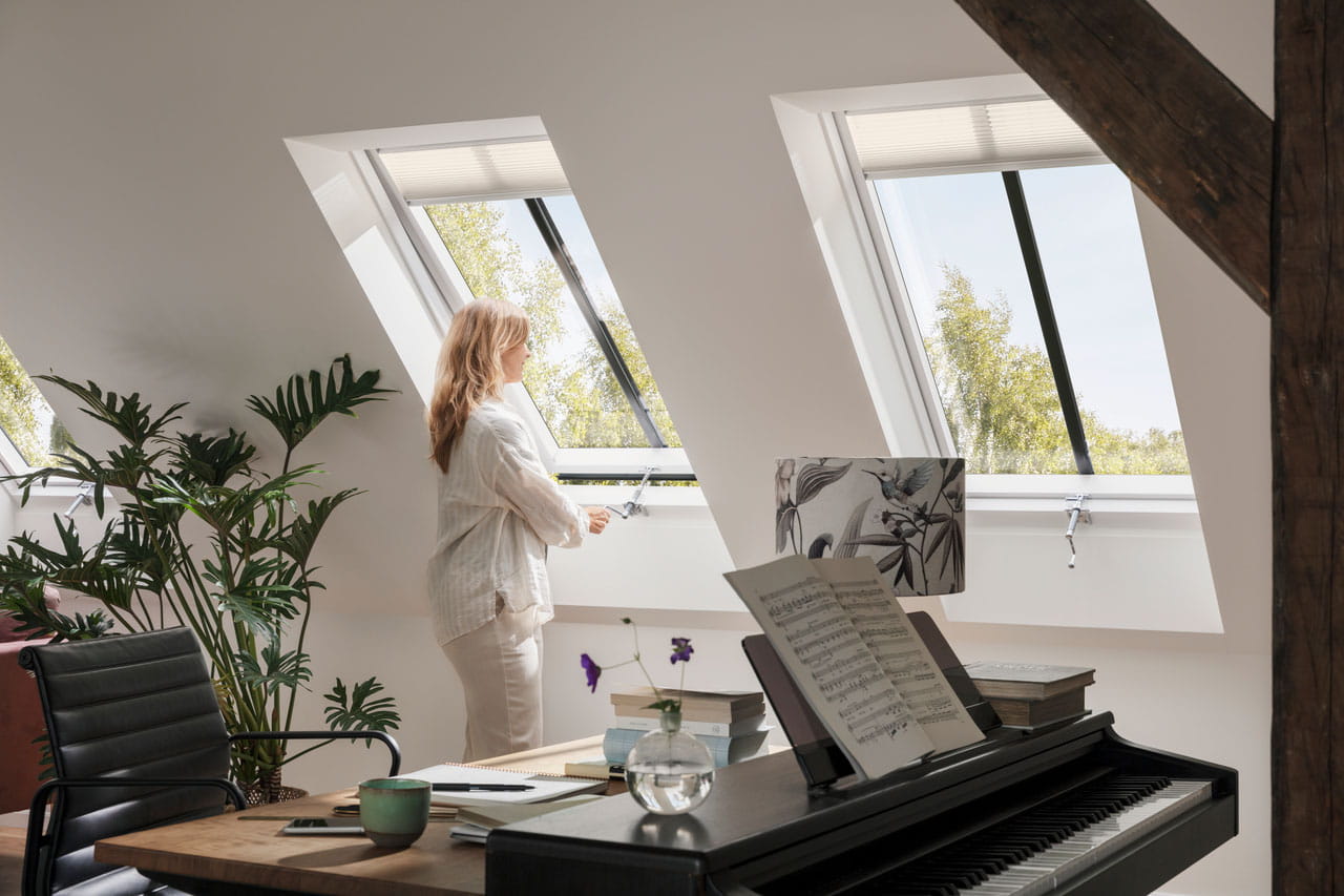 Attic home office with piano, desk, and VELUX roof windows overlooking trees.