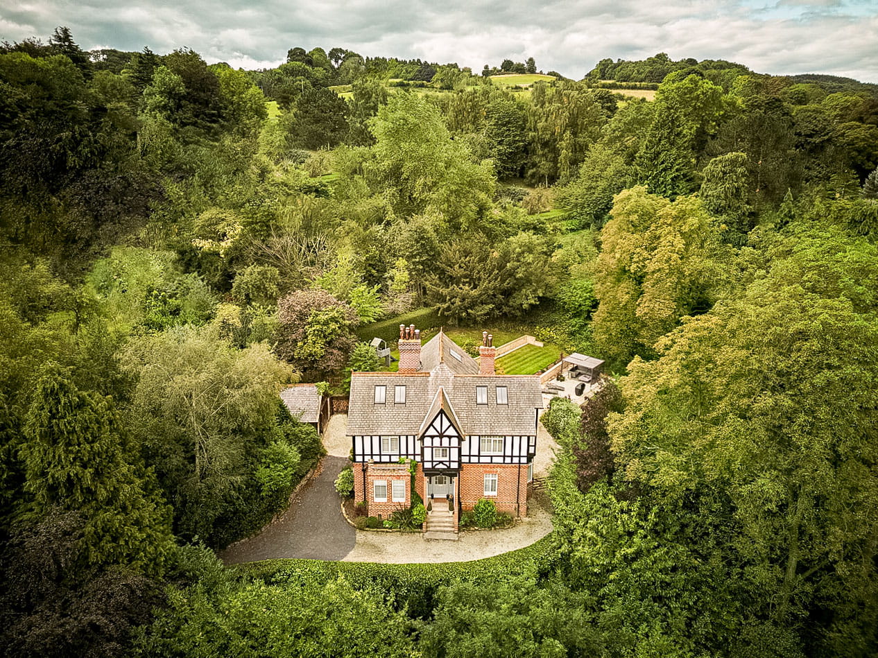Aerial view of a traditional countryside house surrounded by dense green trees.