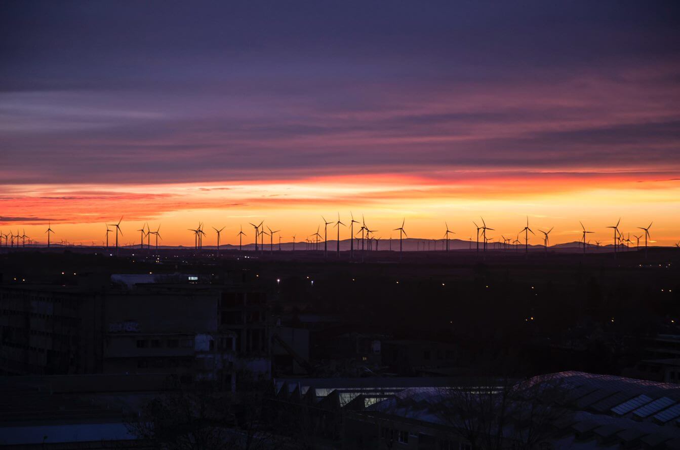 Turbine eoliche contro un cielo di tramonto vivido, simboleggianti l'energia sostenibile.