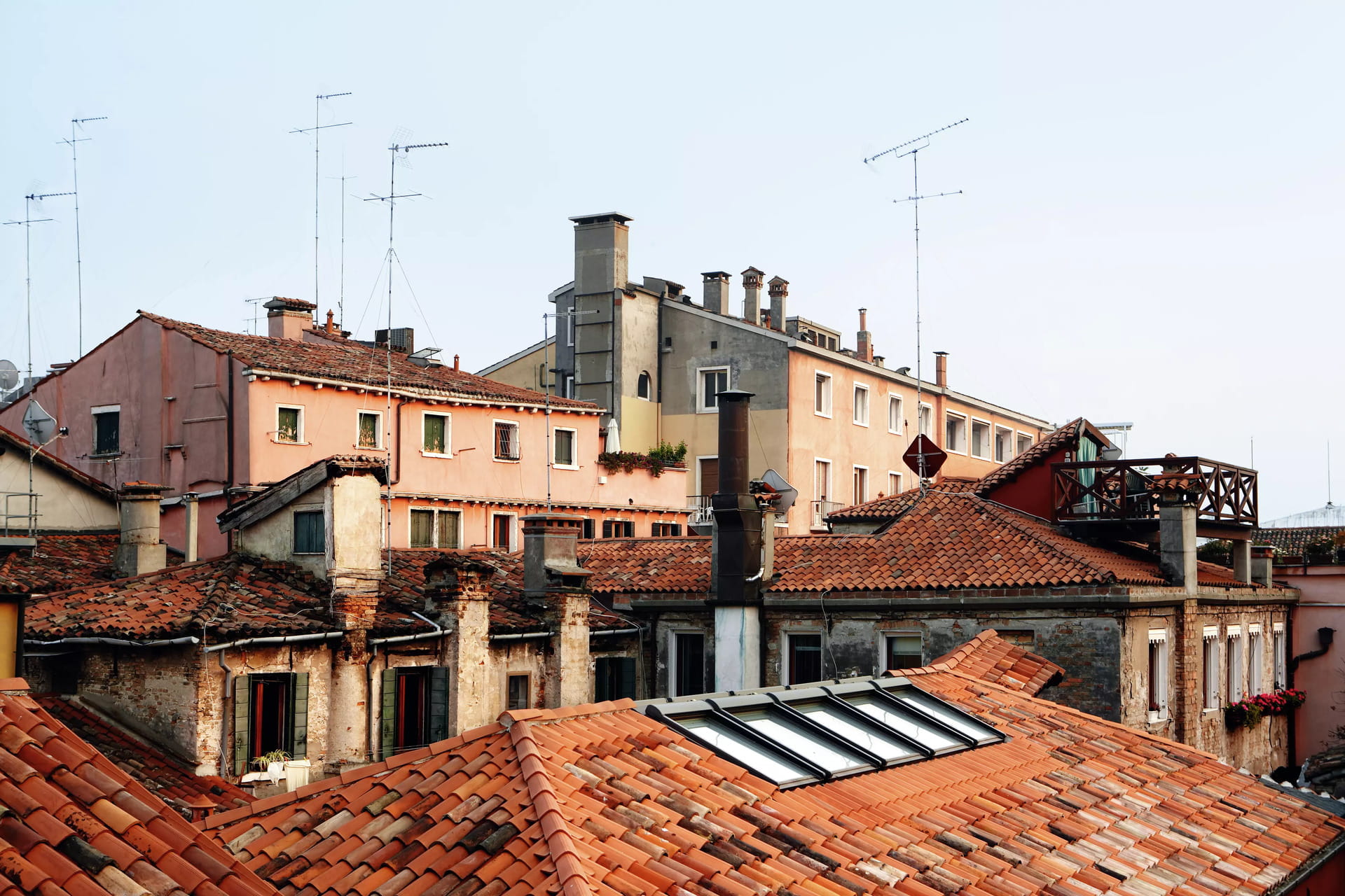 Tetti in terracotta invecchiata con finestre moderne VELUX su uno sfondo di cielo soffice.