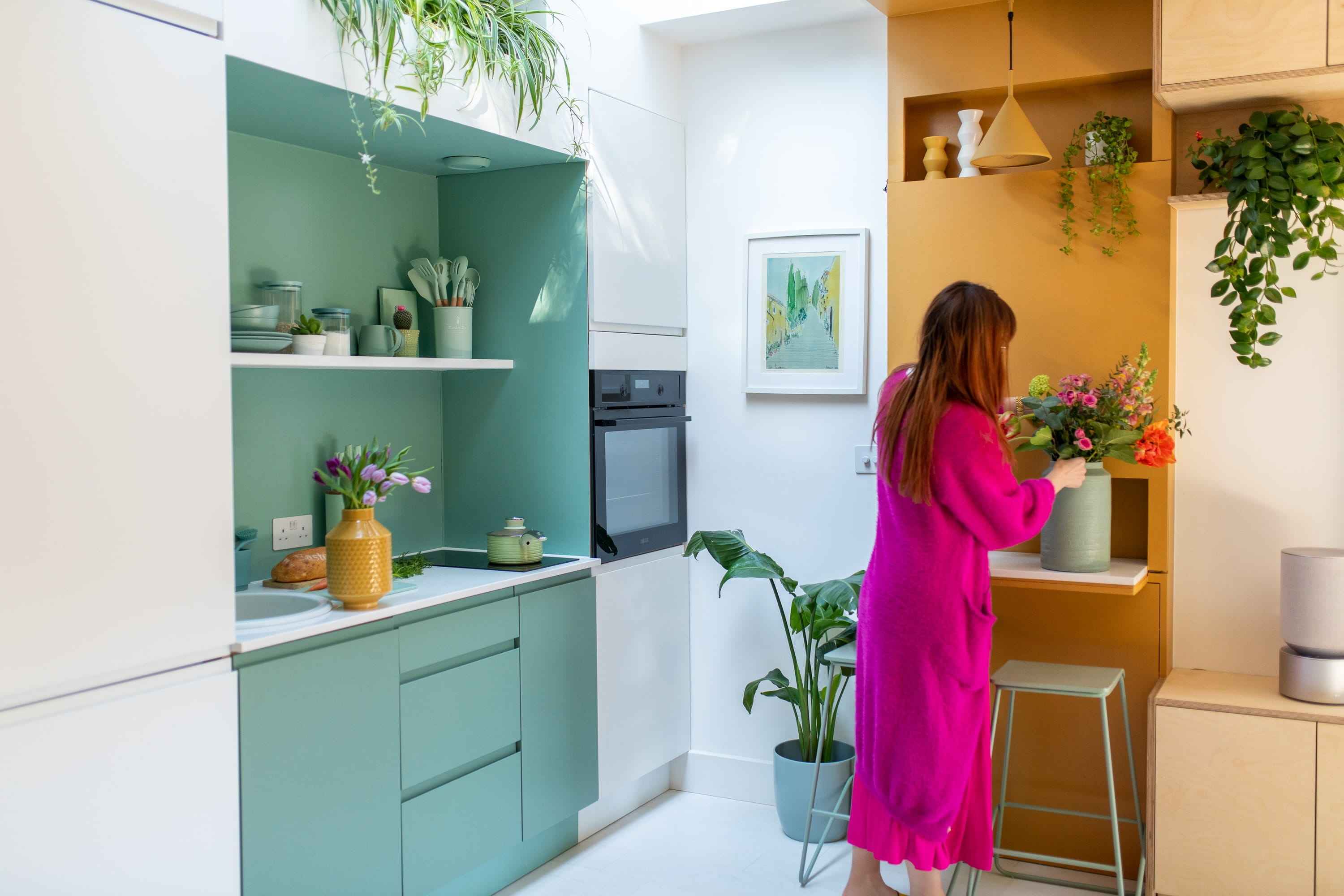 Donna in rosa che sistema fiori in una cucina moderna turchese e gialla con piante.
