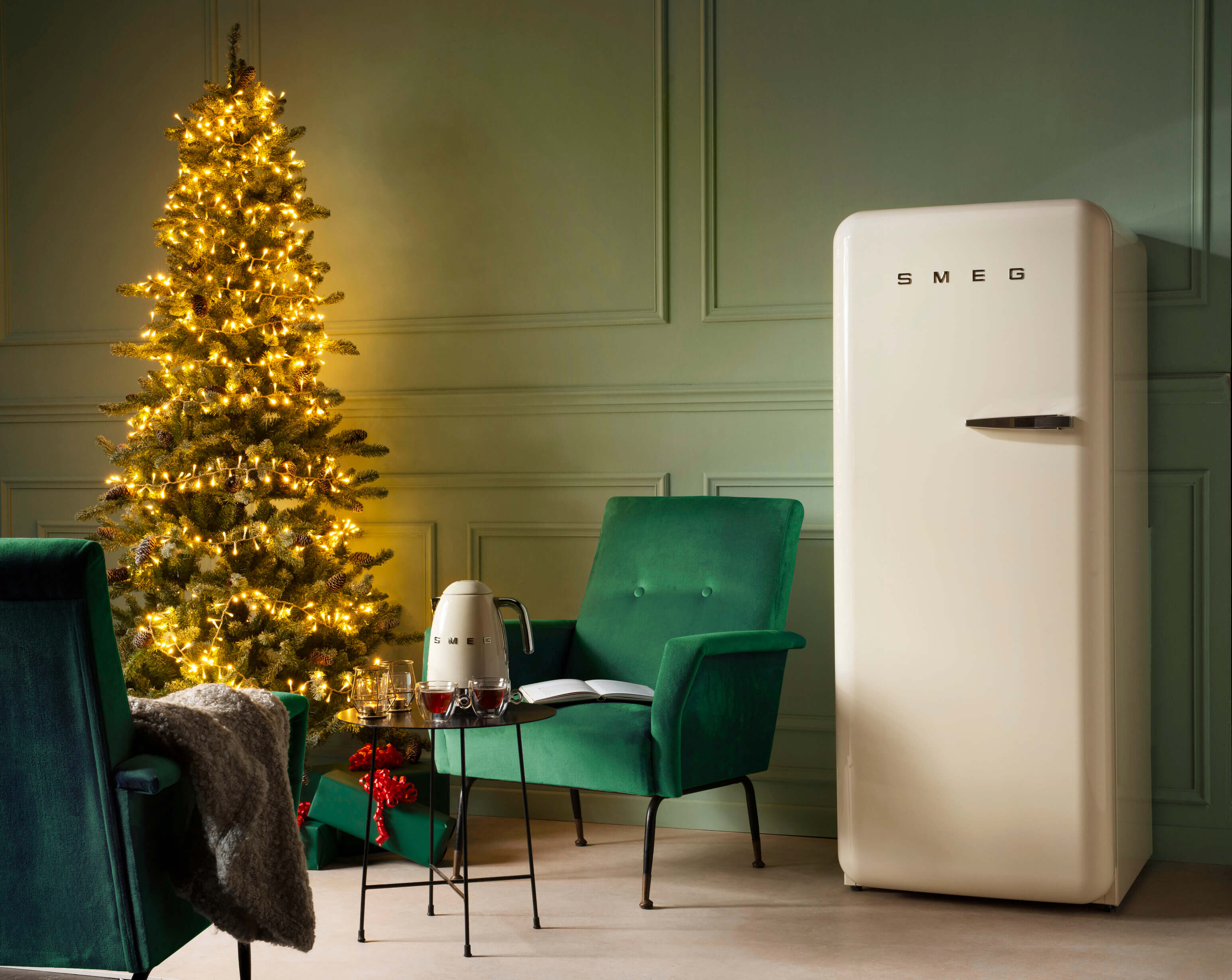 Retro SMEG Kühlschrank in einer festlichen Küche mit einem beleuchteten Weihnachtsbaum und grünen Stühlen.
