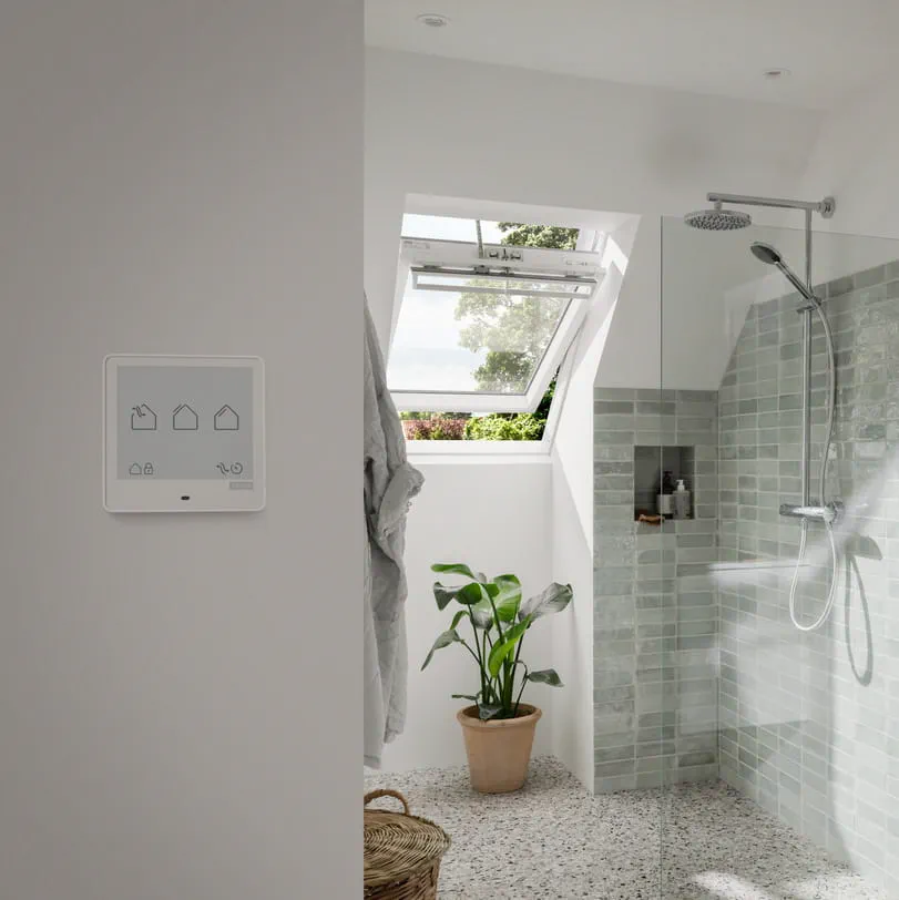 Modernes Badezimmer mit VELUX Dachflächenfenster, grünen Fliesen, Pflanze und intelligentem Kontrollpanel.