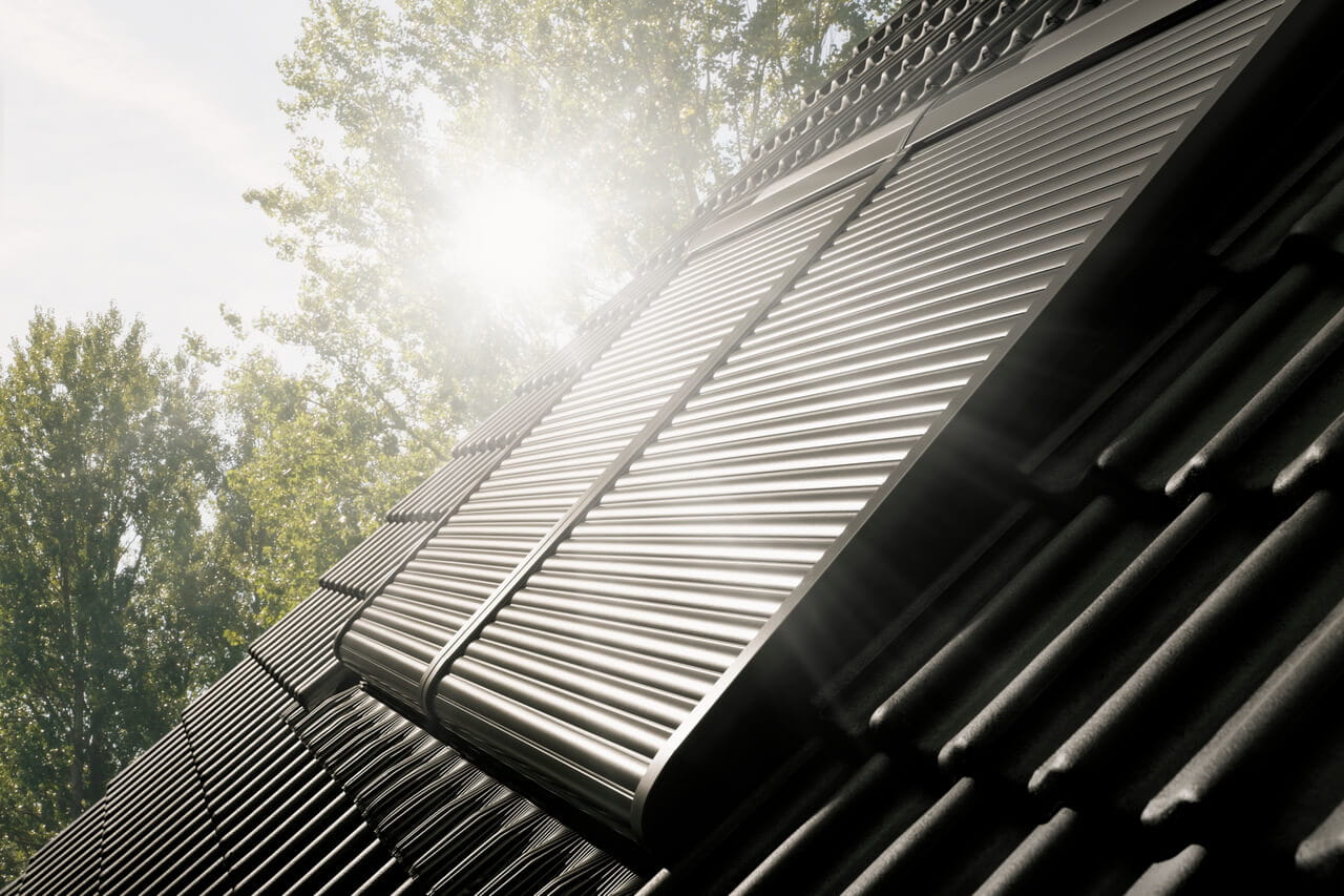 VELUX Dachflächenfenster an einem geneigten Dach mit Sonnenlicht, das durch Bäume filtert.