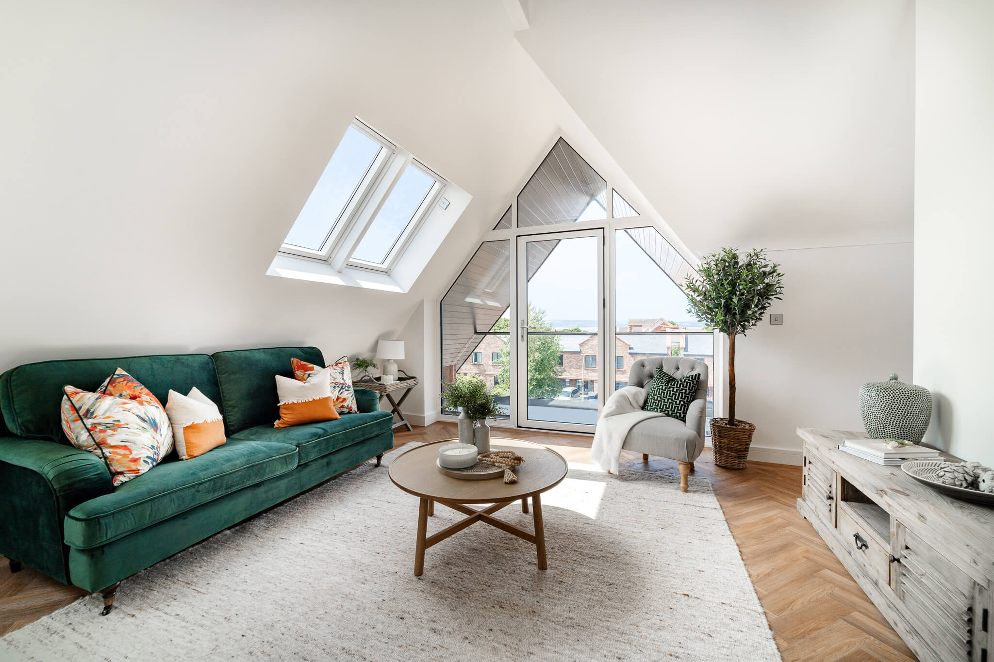 Dachboden-Wohnzimmer mit VELUX-Fenstern, grünem Sofa und städtischer Aussicht.