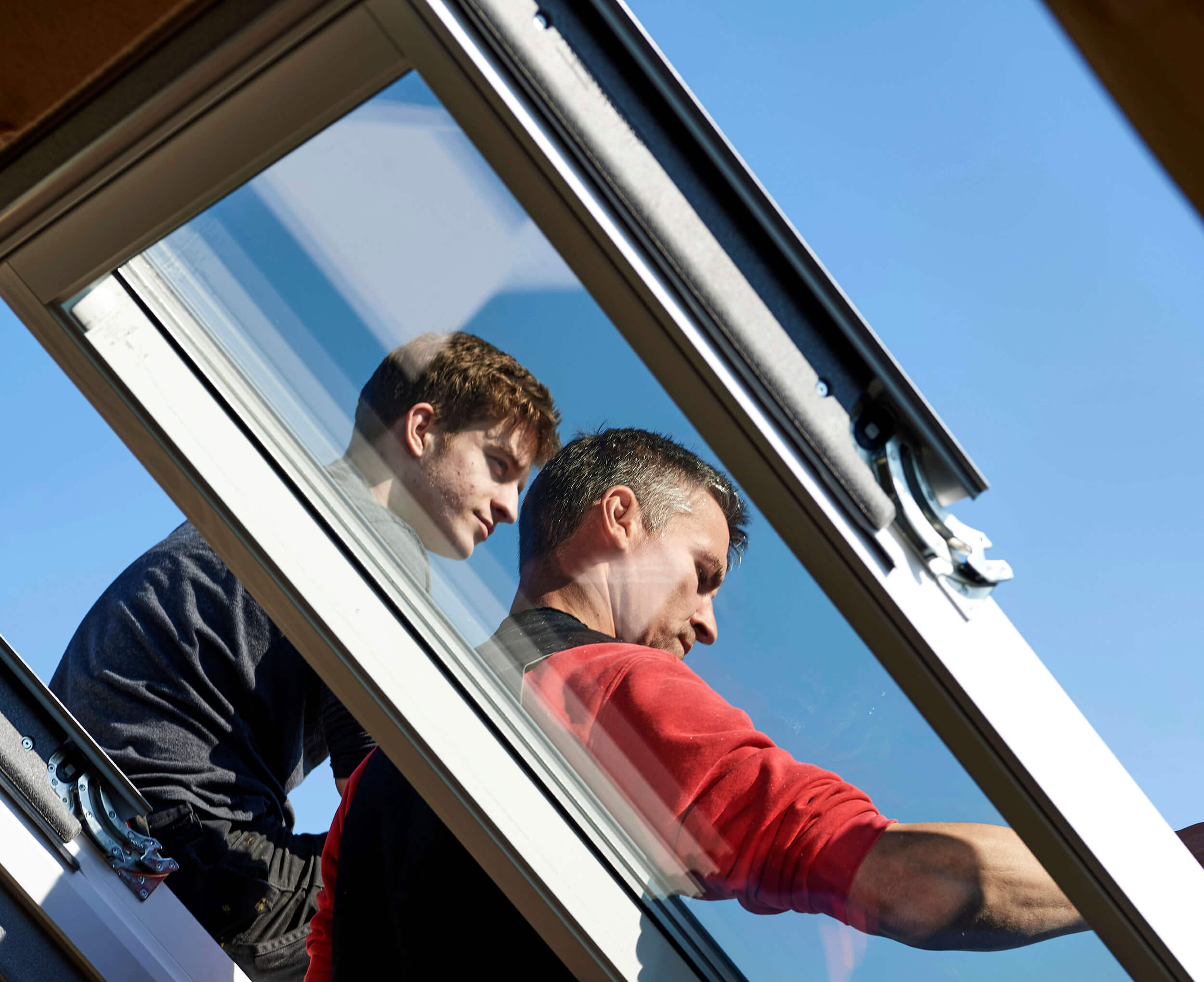Fachleute installieren ein VELUX Dachflächenfenster gegen einen klar blauen Himmel.