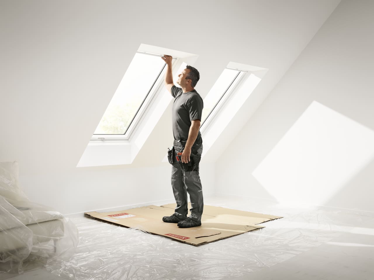Einbauer montiert ein VELUX Dachflächenfenster in einem hellen Dachbodenraum.