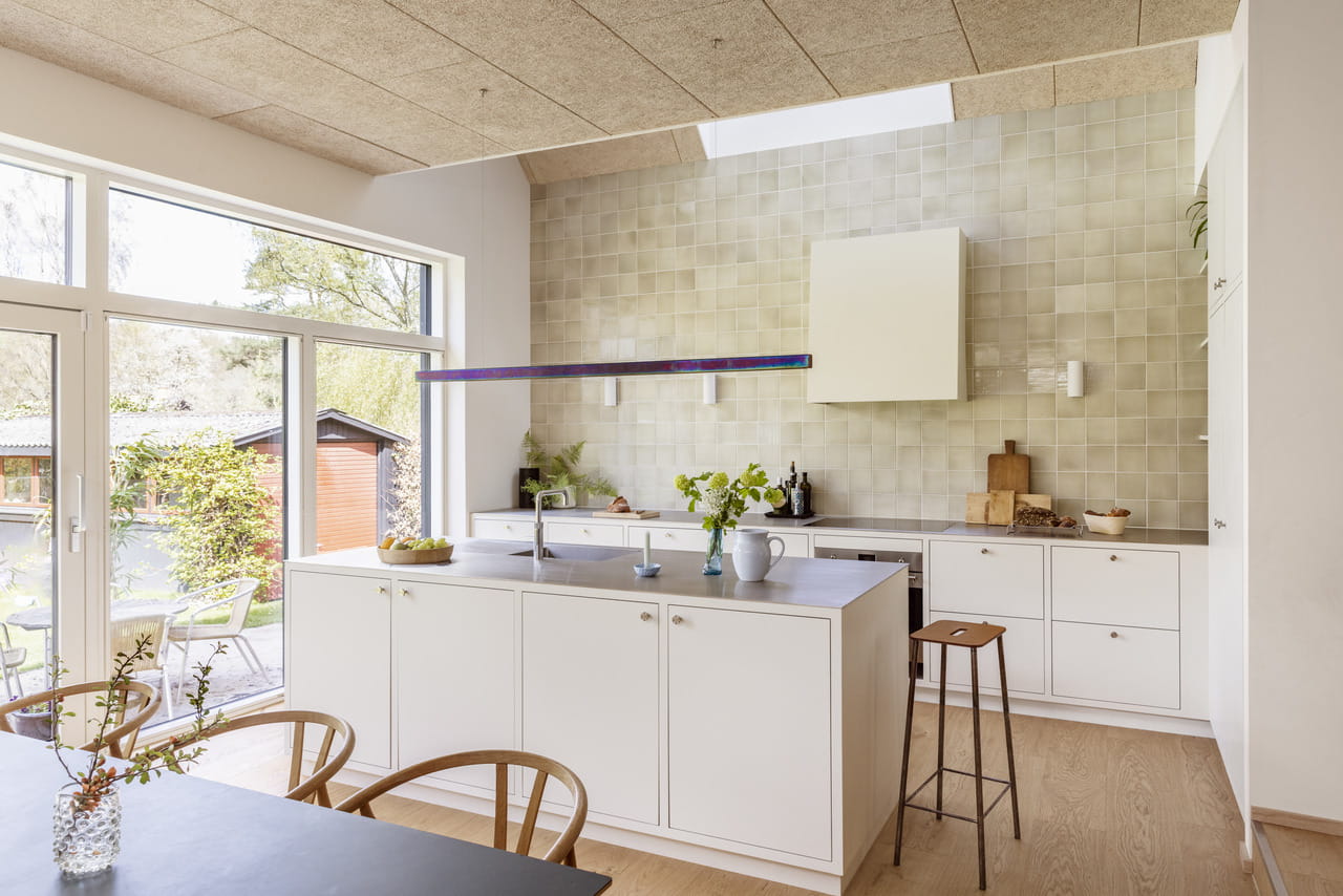 Moderne Küche mit weißen Schränken, zentraler Insel und VELUX Dachflächenfenster, das für reichlich Licht sorgt.