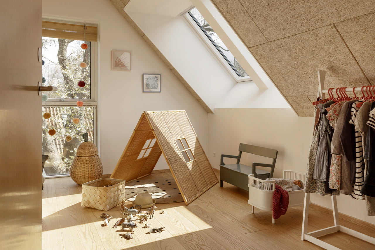 Dachboden-Spielzimmer mit natürlichem Licht durch ein VELUX Dachflächenfenster, hölzerne Spielzeuge und ein Spielhaus.