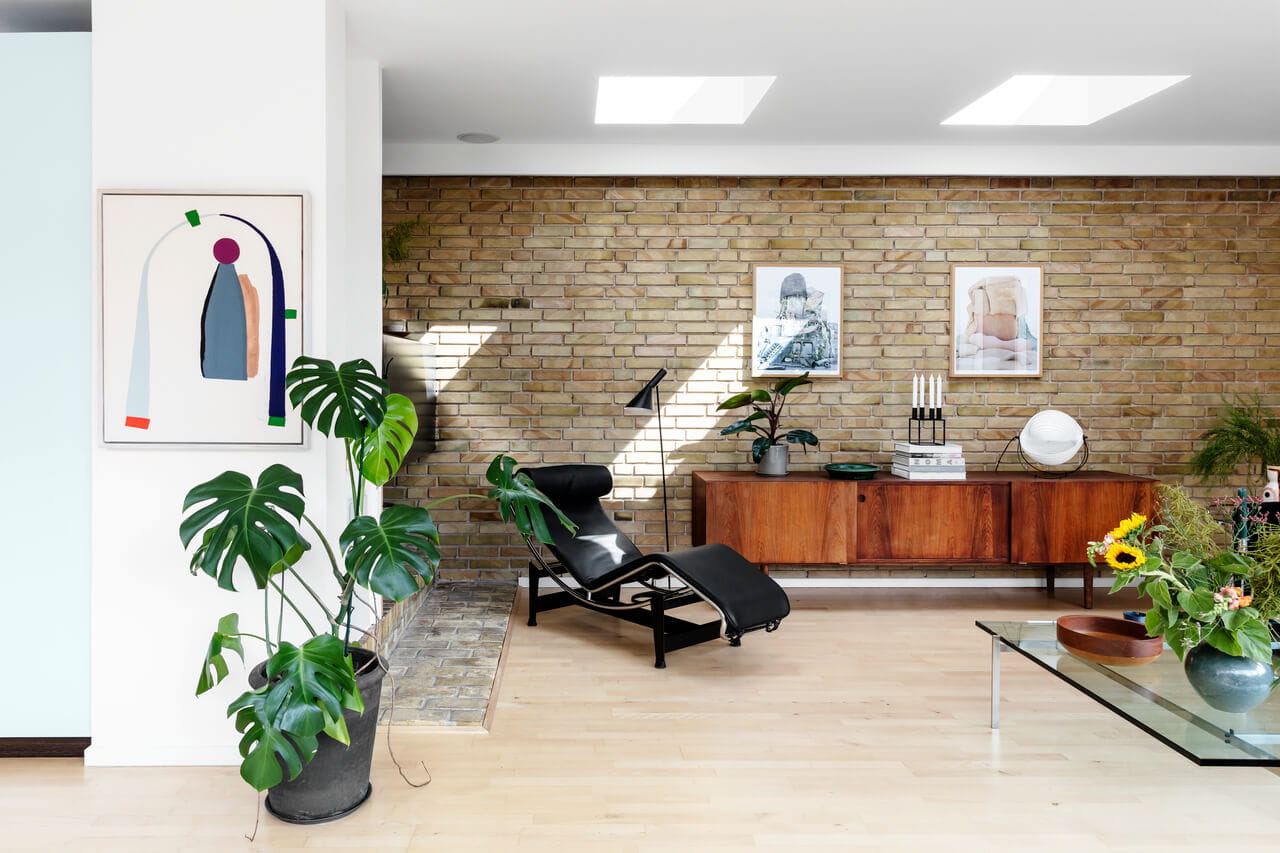 Moderne stue med murstensvæg, sort chaiselong, glasbord, planter og VELUX ovenlysvinduer.