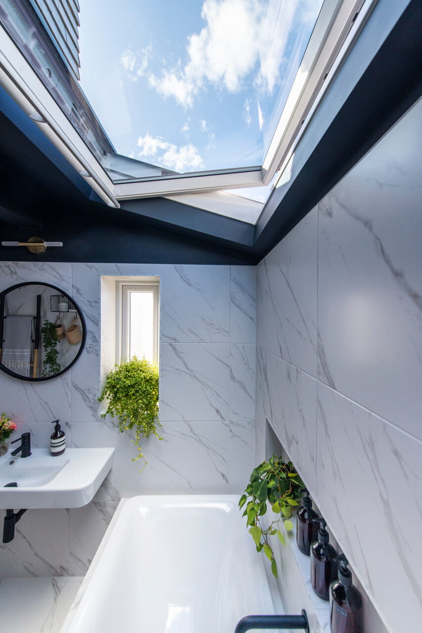 A bathtub with an open roof window just above it.