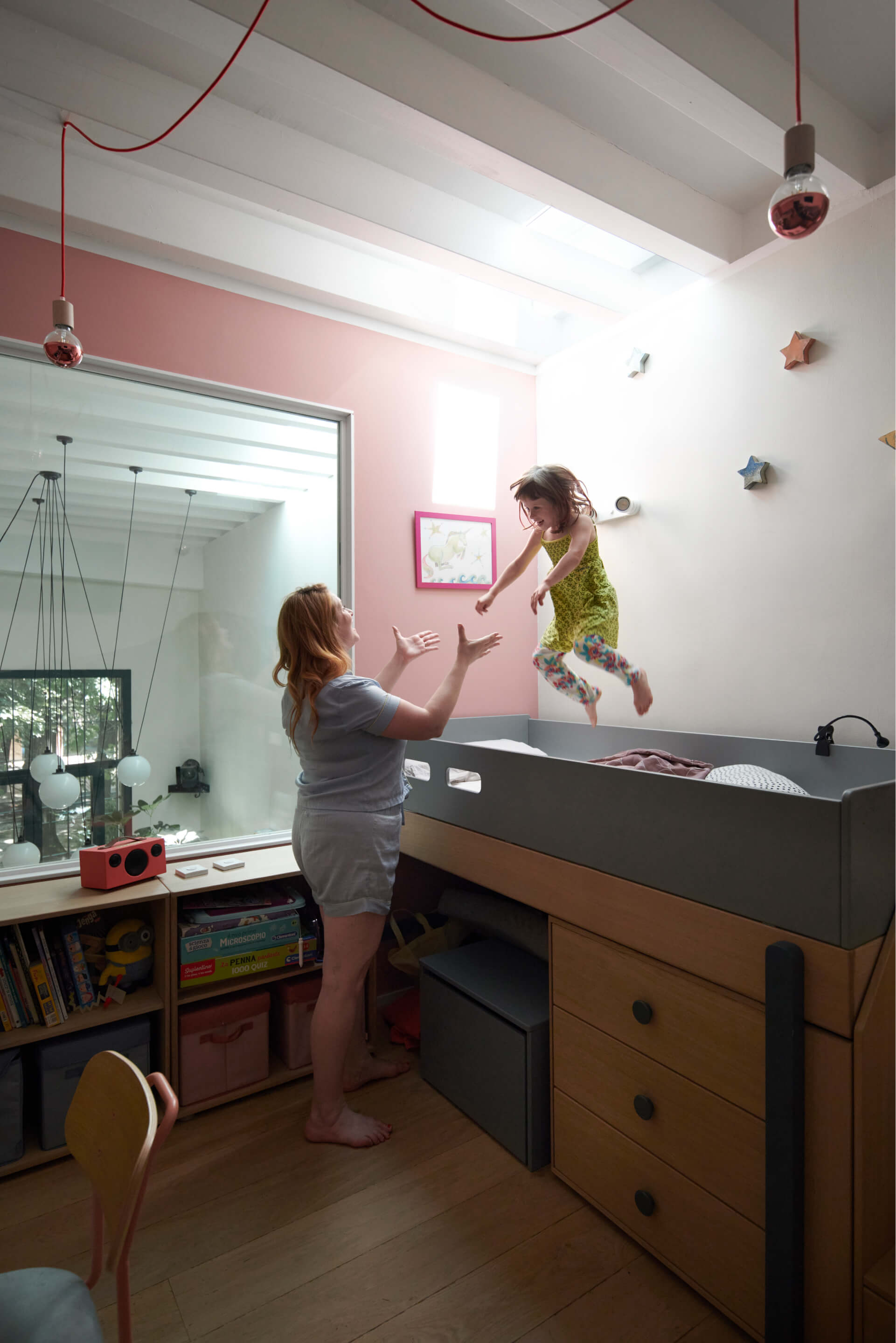 Woman standing by the kids bead, while kid is jumping on the bed.