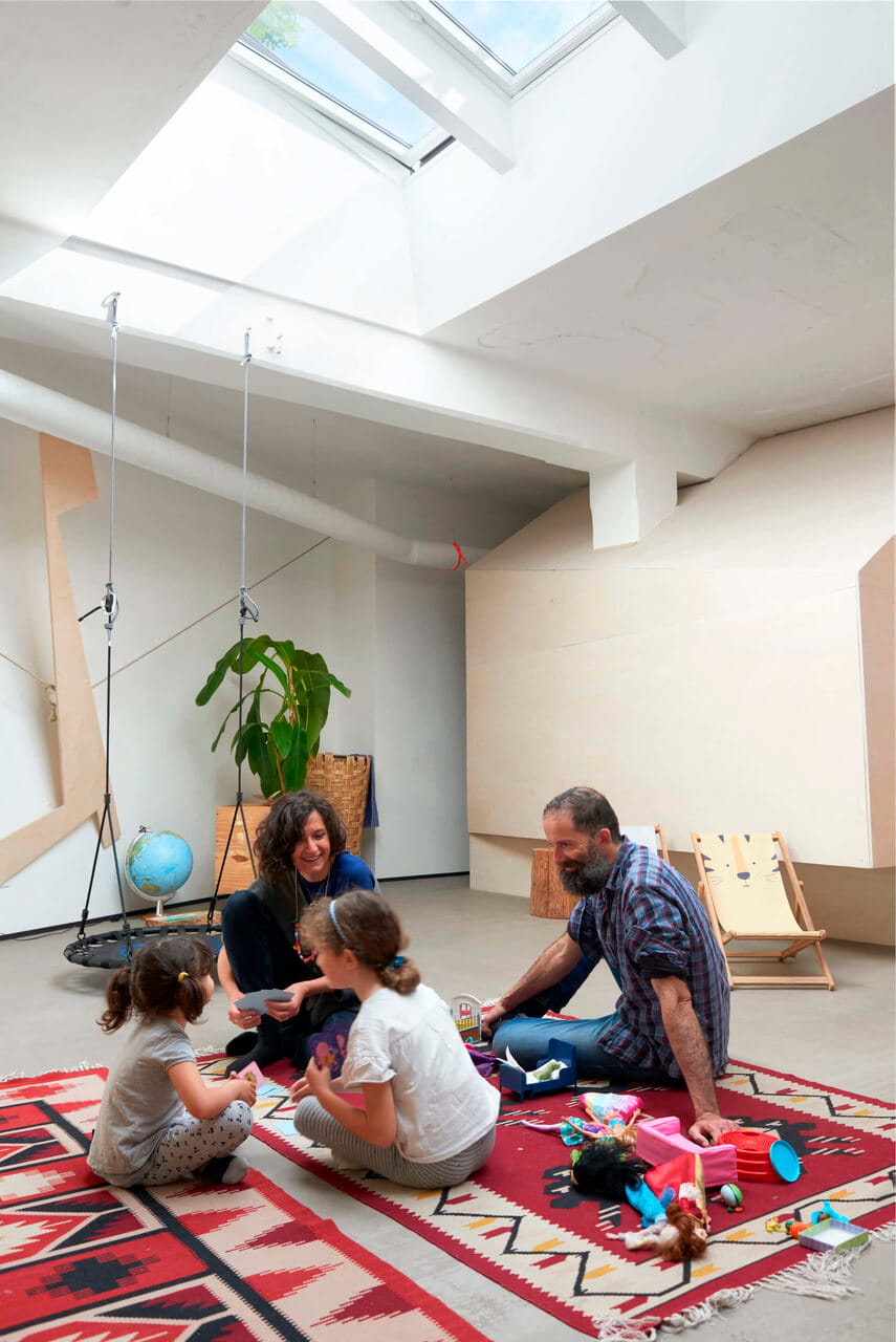 Man, woman and two kids playing on the carpet in the bright room under the roof window