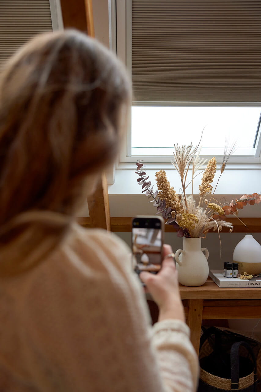 Woman taking a photo on mobile of the flowers that stand on the table.
