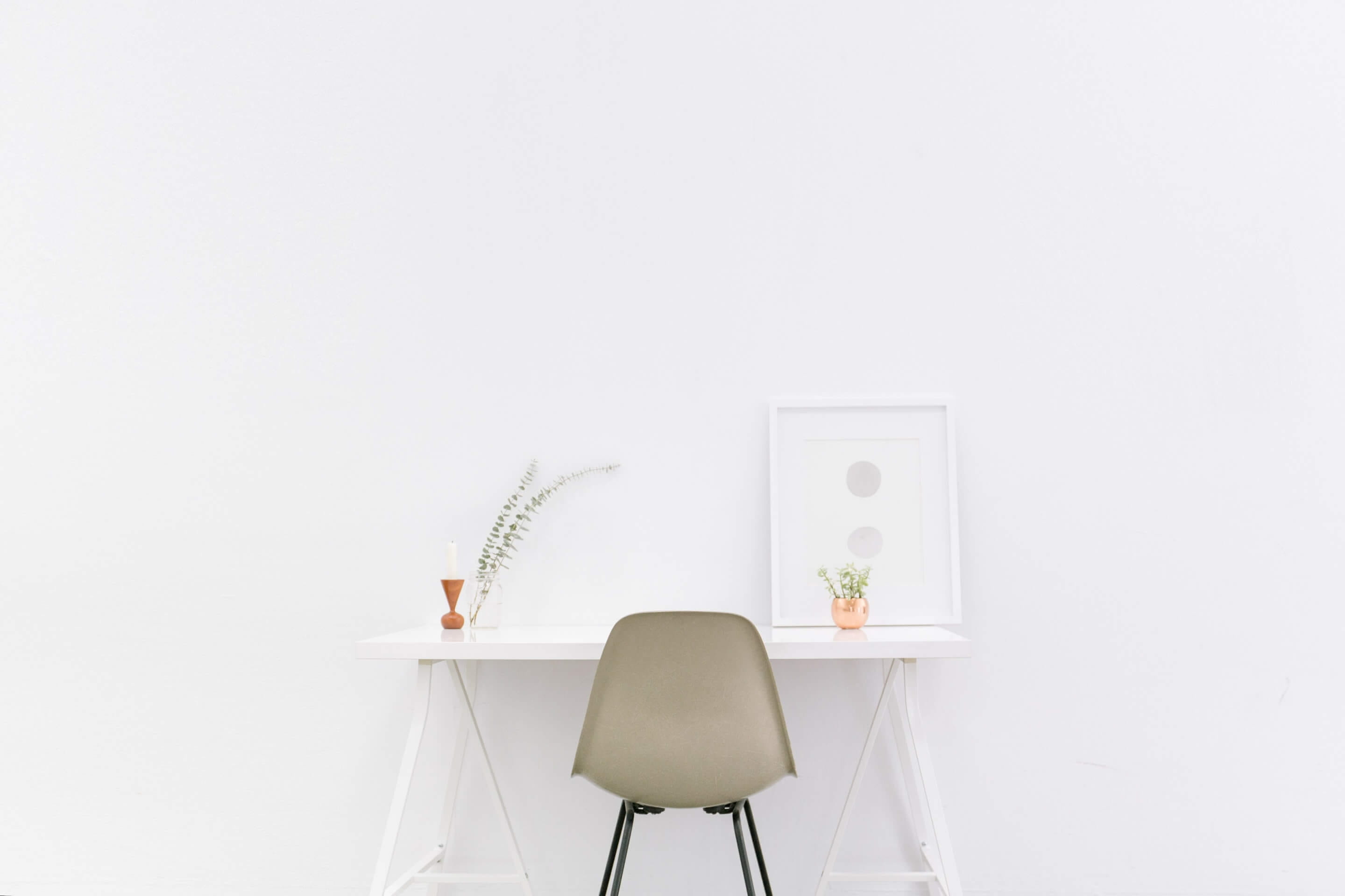 Minimalistisches weißes Homeoffice mit grünem Stuhl und kleinen Schreibtischpflanzen.